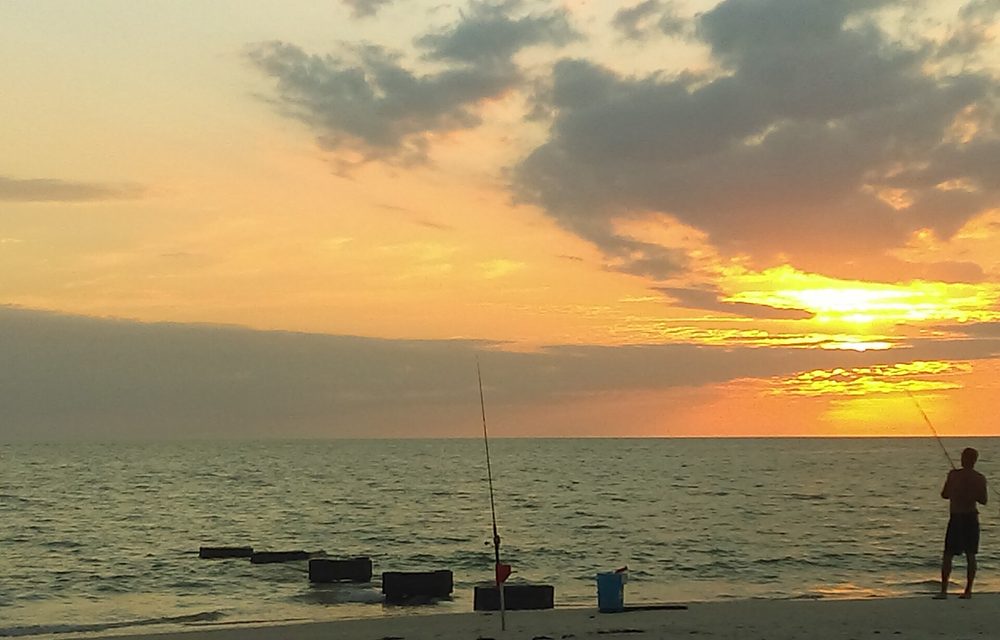 Angler silhouetted against a golden sunset in Naples